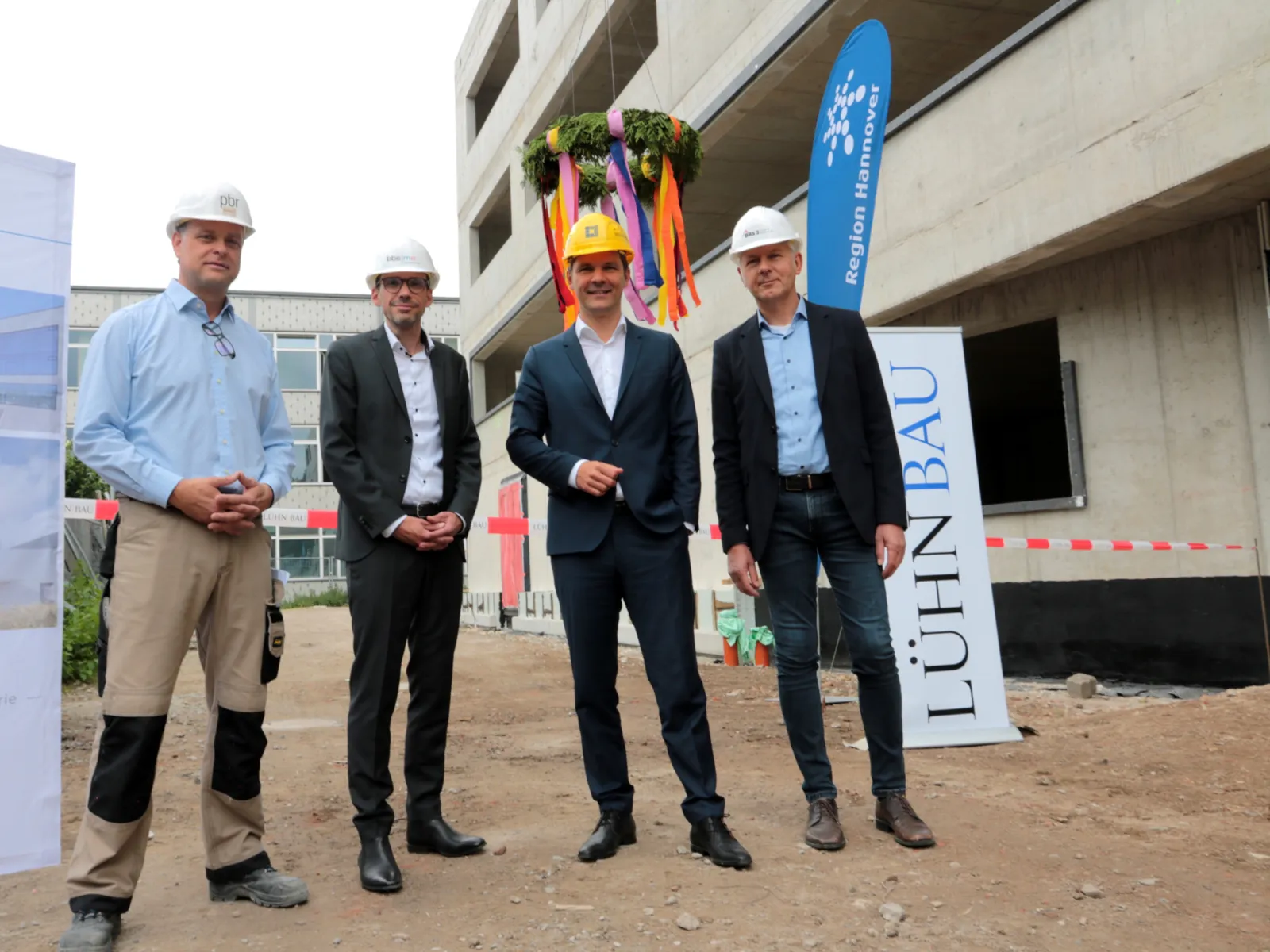 Gruppenbild auf einer Baustelle. Im Hintergrund hängt eine Richtkranz.